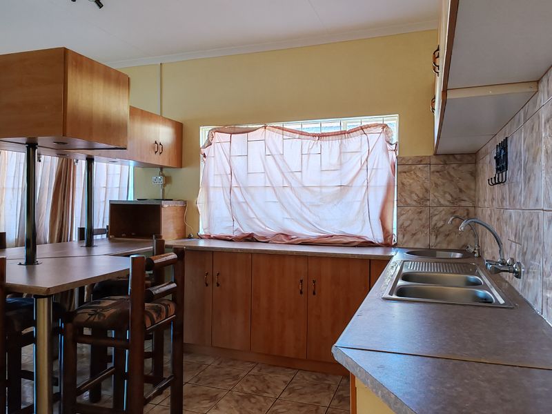 A functional kitchen featuring laminate cabinetry, a double bowl stainless steel sink, and a breakfast bar, offering a practical layout with potential for modernization.