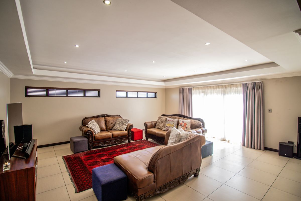 Spacious living room featuring recessed tray ceilings with integrated downlighting, large format floor tiles, and sliding glass doors leading to the exterior.