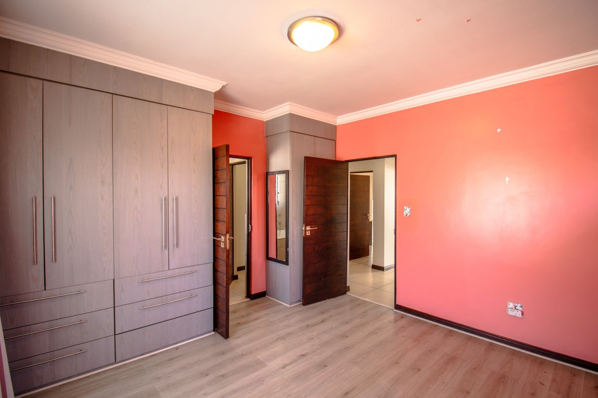 A well-maintained bedroom featuring built-in grey cabinetry, laminate wood flooring, and access to adjacent rooms through solid timber doors.