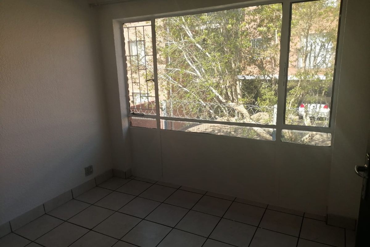An empty bedroom featuring large windows with security bars, tiled flooring, and neutral wall finishes, offering a bright and functional living space.