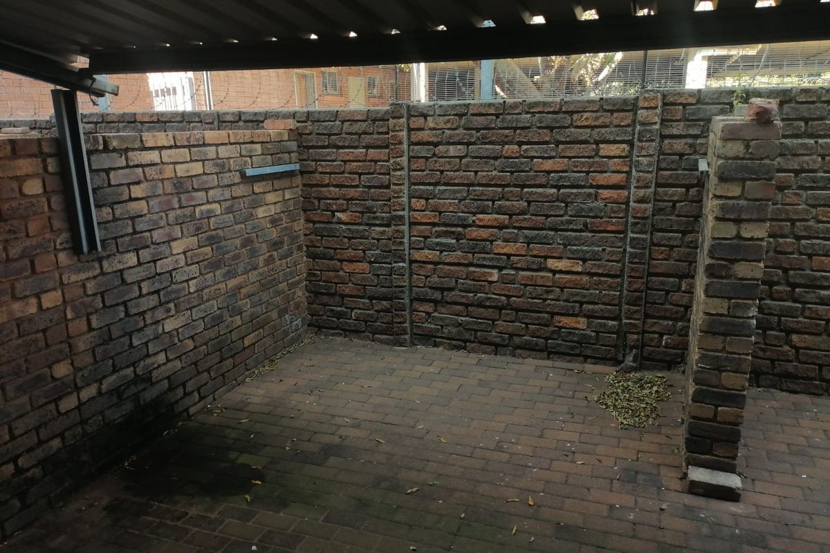 A private, enclosed courtyard area featuring exposed brick walls and paved flooring, covered by a corrugated metal roof structure.