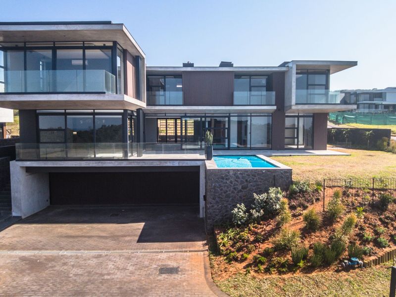 Modern multi-level luxury residence featuring a cantilevered design, glass balustrades, a private swimming pool, and extensive floor-to-ceiling glazing overlooking the landscaped grounds.