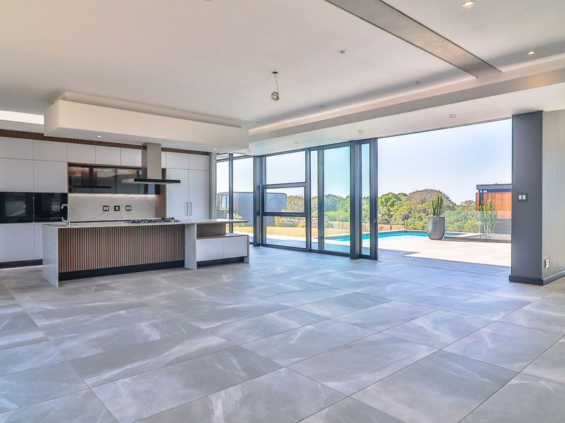 Spacious open-plan kitchen and living area featuring modern cabinetry, stone countertops, large format floor tiles, and seamless indoor-outdoor flow to the pool deck.