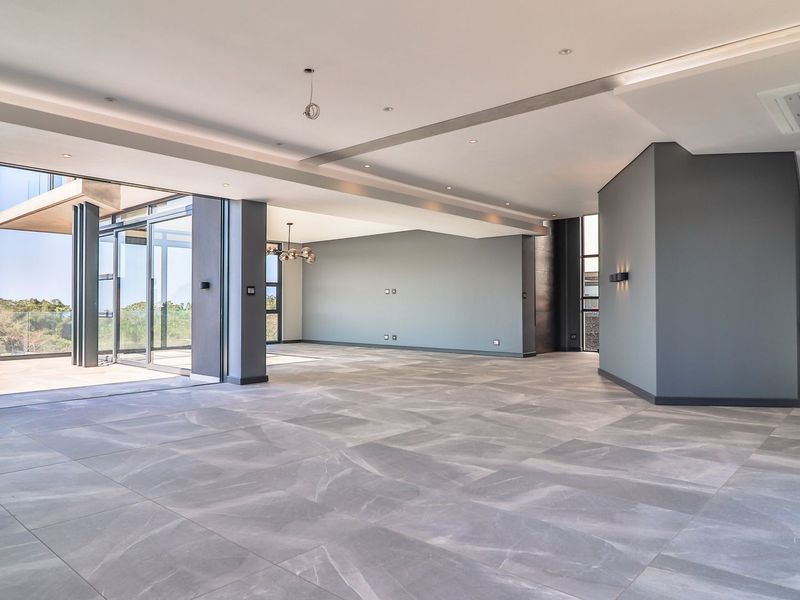 Spacious open-plan living area featuring large format floor tiles, recessed lighting, and expansive sliding glass doors leading to an outdoor patio.