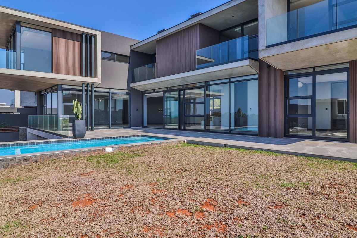 Modern double-story residence featuring expansive glass sliding doors, concrete balconies with glass balustrades, and a private swimming pool overlooking the rear garden.