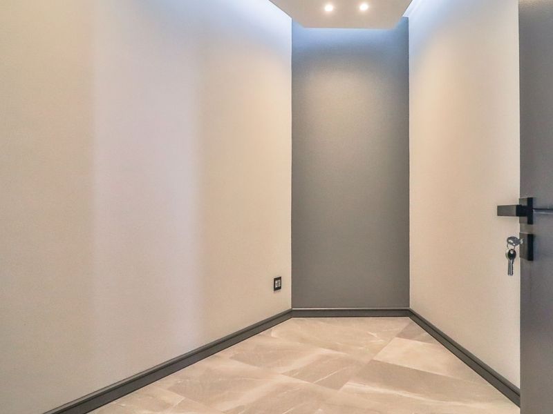 A clean, modern entrance foyer featuring neutral wall tones, recessed ceiling lighting, and polished tiled flooring.