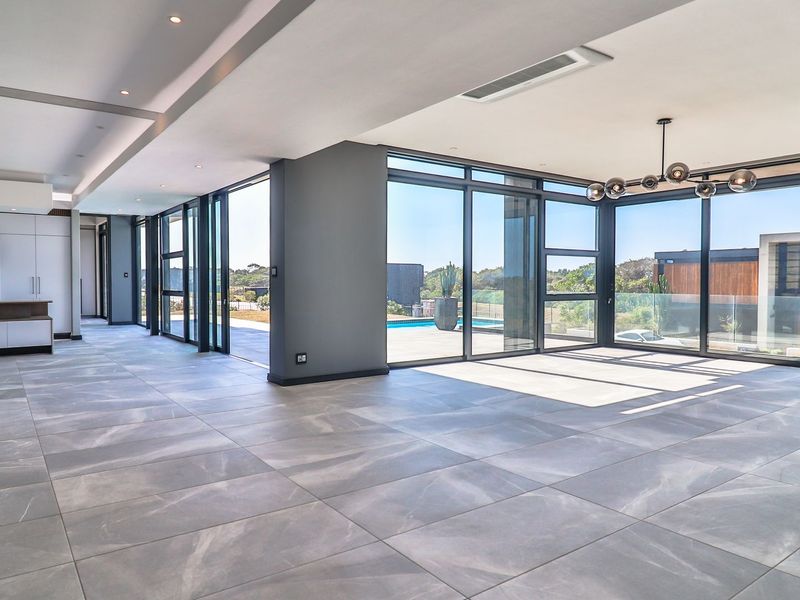 Spacious open-plan living and kitchen area featuring large format floor tiles, floor-to-ceiling sliding doors, and modern integrated kitchen cabinetry with recessed lighting.