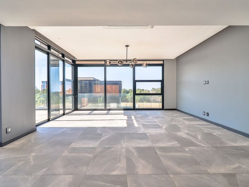Spacious, modern living area featuring large format floor tiles, expansive floor-to-ceiling glass sliding doors, and contemporary lighting, offering seamless indoor-outdoor flow.