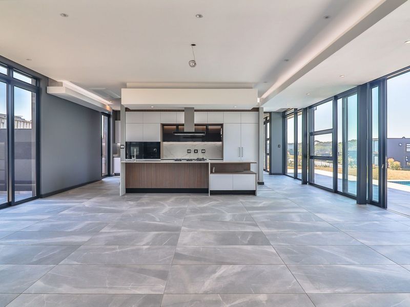 Spacious open-plan living and kitchen area featuring modern cabinetry, a central island, large format floor tiles, and expansive sliding glass doors leading outdoors.