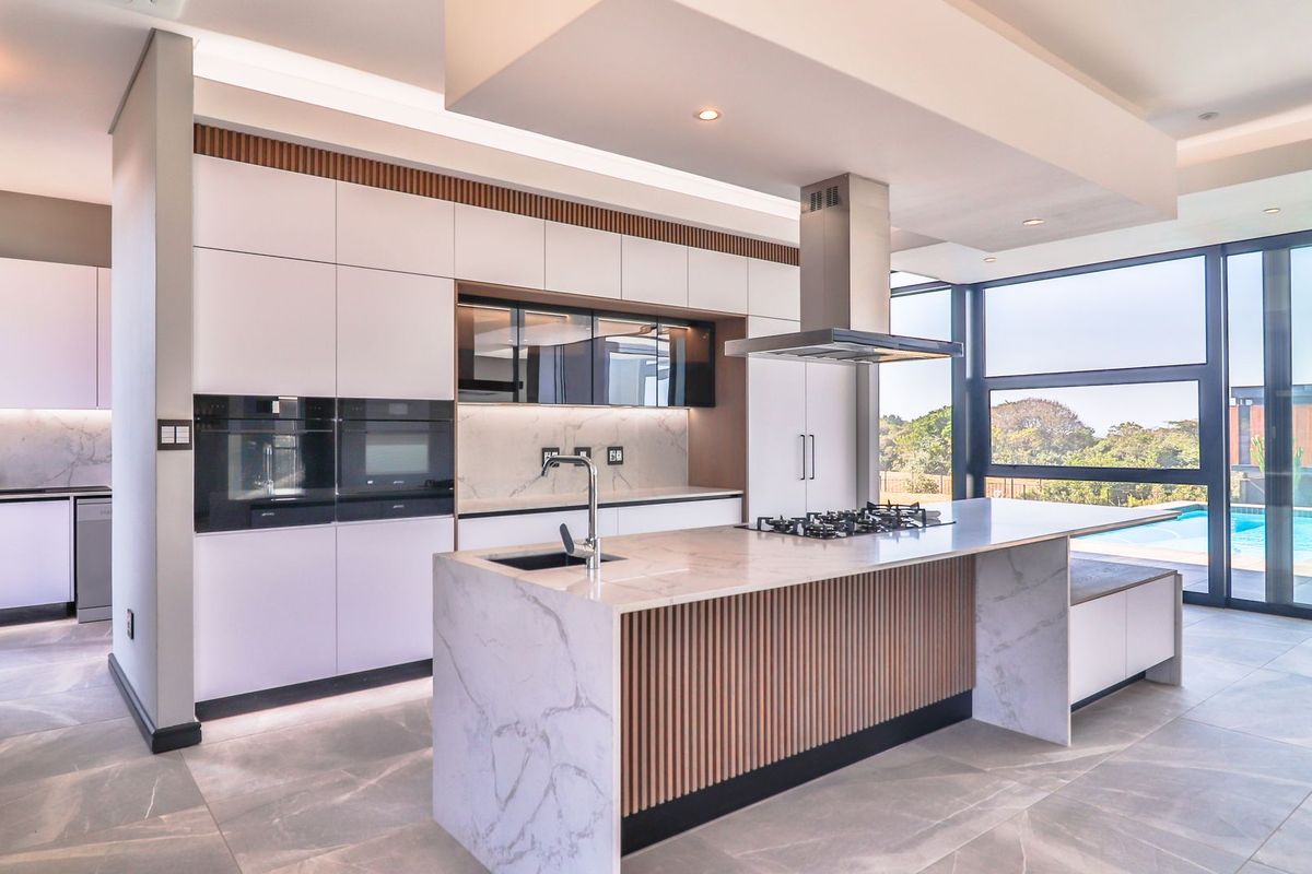 Modern luxury kitchen featuring a marble island, integrated appliances, sleek cabinetry, and floor-to-ceiling windows with views of the pool area.