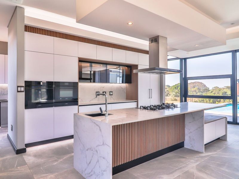 Modern luxury kitchen featuring a marble island, integrated appliances, sleek cabinetry, and floor-to-ceiling windows with views of the pool area.