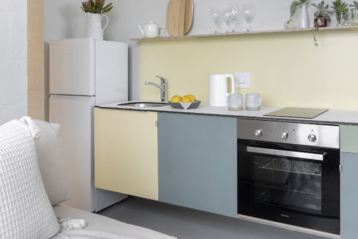 Compact kitchenette featuring a built-in oven, stainless steel sink, and pastel-toned cabinetry, integrated into an open-plan living space.