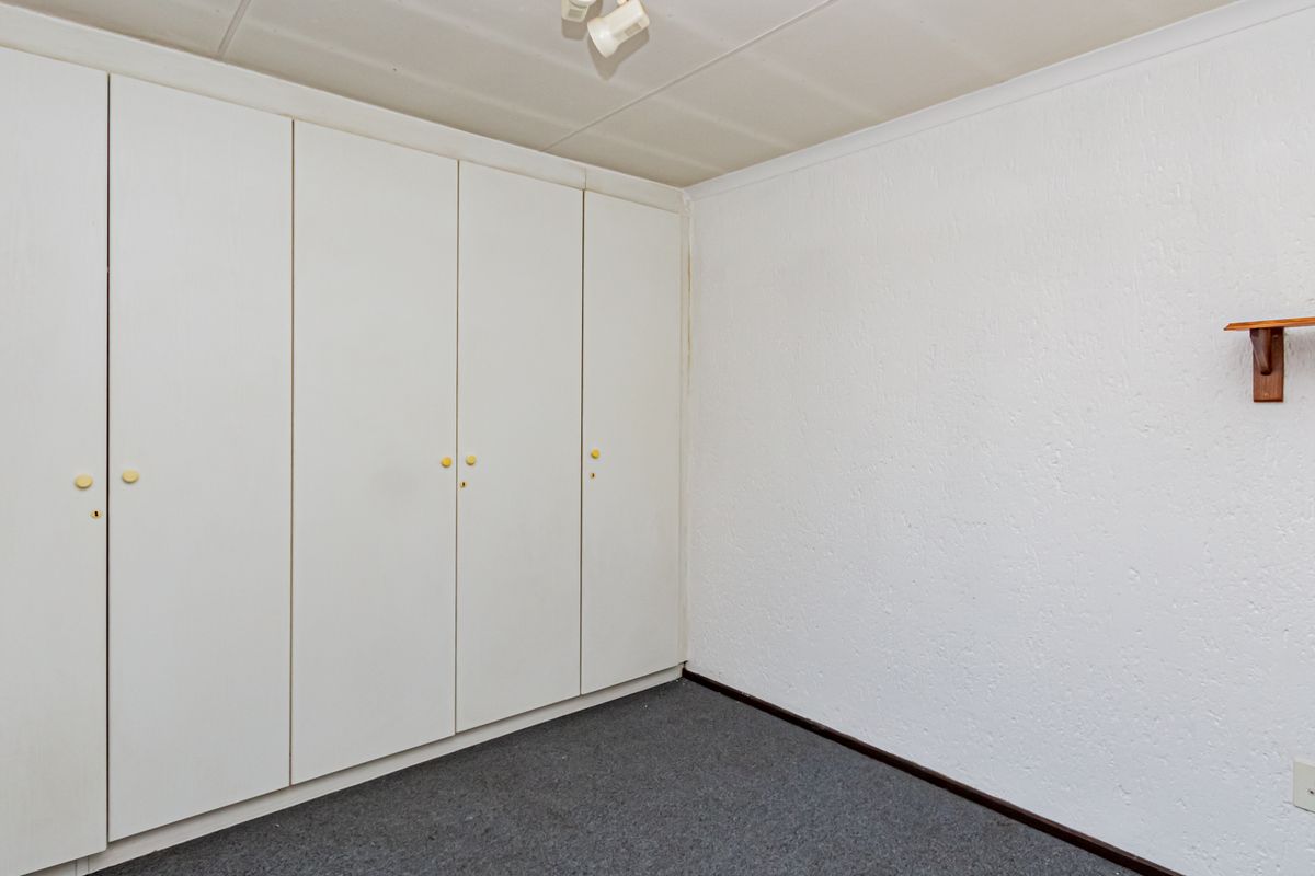 A bedroom featuring built-in white cabinetry, grey carpeting, and a simple wall-mounted shelf.