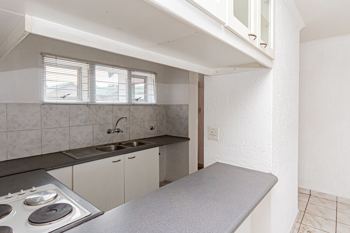 A functional kitchen featuring a built-in electric hob, double sink, laminate countertops, and overhead cabinetry with a breakfast bar area.
