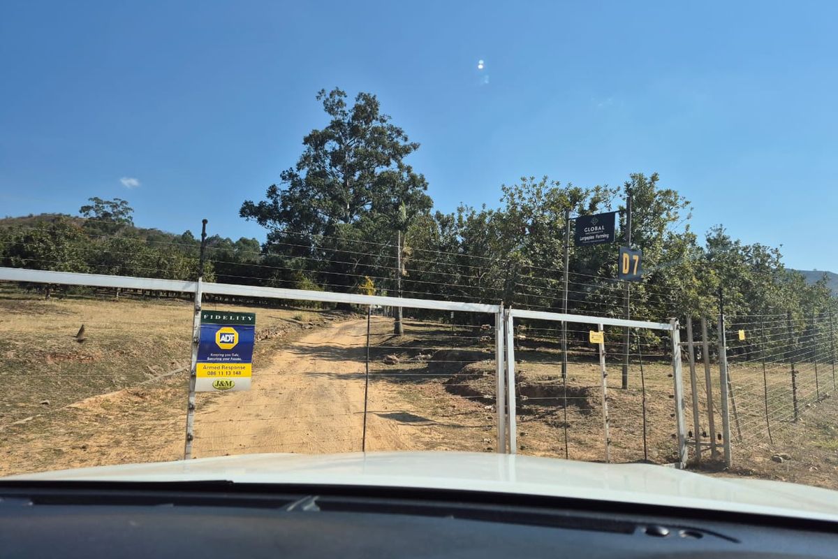 Entrance to the farm property featuring a metal gate, electric fencing, and a dirt driveway leading into the landscape.