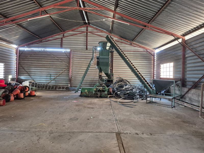 Large industrial-style utility shed featuring a high-pitched corrugated metal roof, steel truss framework, and durable concrete flooring, suitable for agricultural or storage purposes.