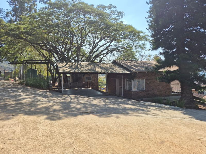 Front exterior view of a brick farmhouse featuring a large concrete driveway, covered carport area, and mature trees on the property.