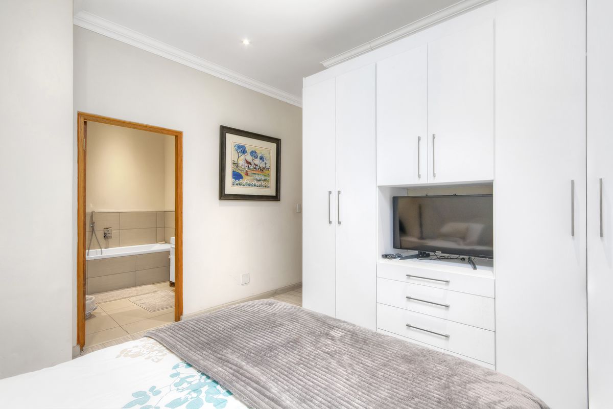 A well-maintained bedroom featuring built-in white cabinetry and an en-suite bathroom with a bathtub.