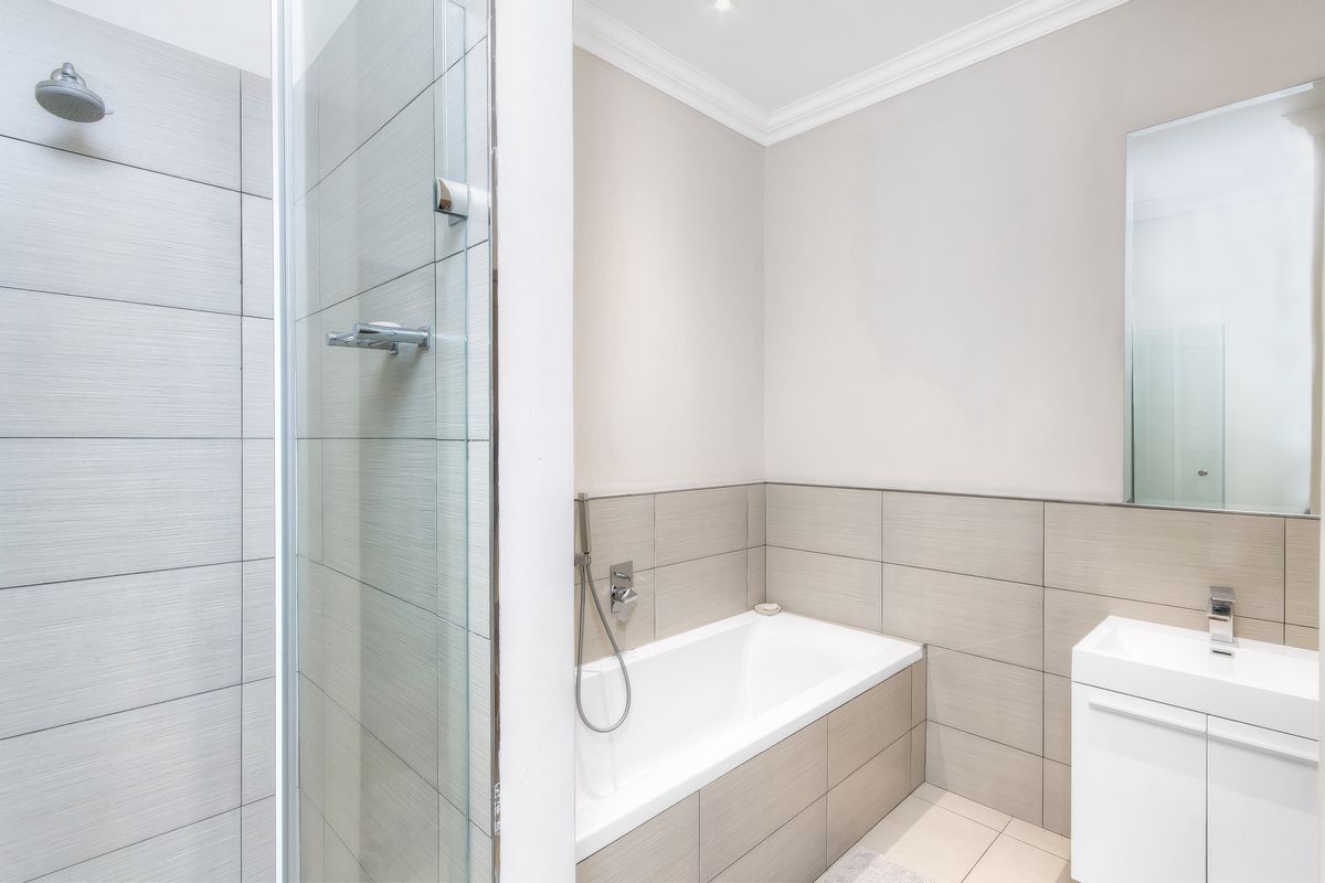 Modern bathroom featuring a glass-enclosed shower, a built-in bathtub with handheld showerhead, and a sleek vanity unit with a wall-mounted mirror.
