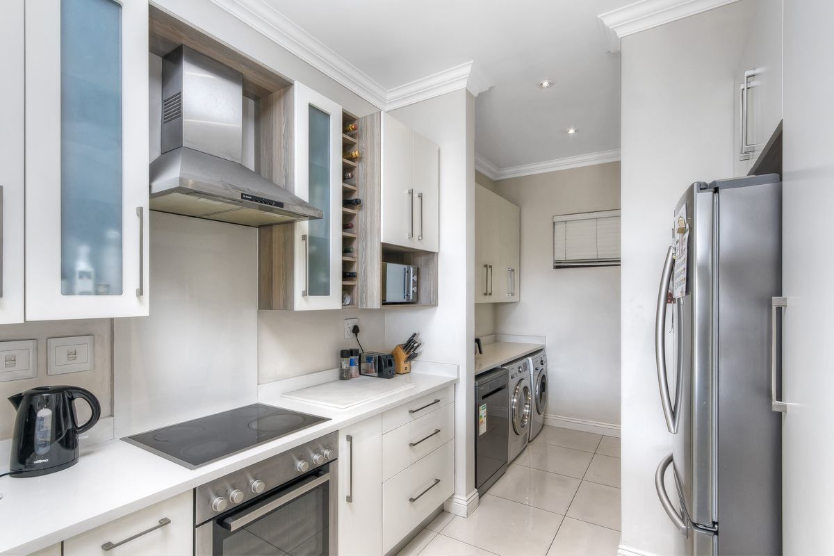 Modern kitchen featuring sleek cabinetry, built-in oven, electric hob, and extractor fan, with an adjoining scullery area for laundry and additional storage.