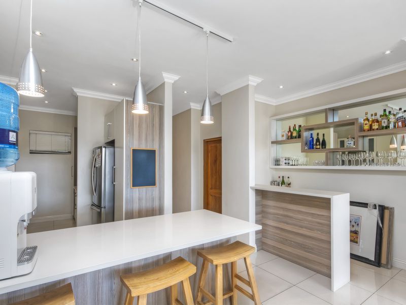 Modern open-plan living area featuring a built-in bar with integrated shelving, sleek tiled flooring, and contemporary pendant lighting throughout the space.