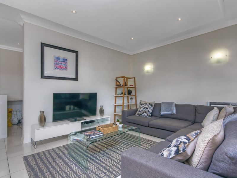 A well-maintained living room featuring tiled flooring, recessed downlighting, and modern wall-mounted light fixtures, creating a bright and comfortable living space.