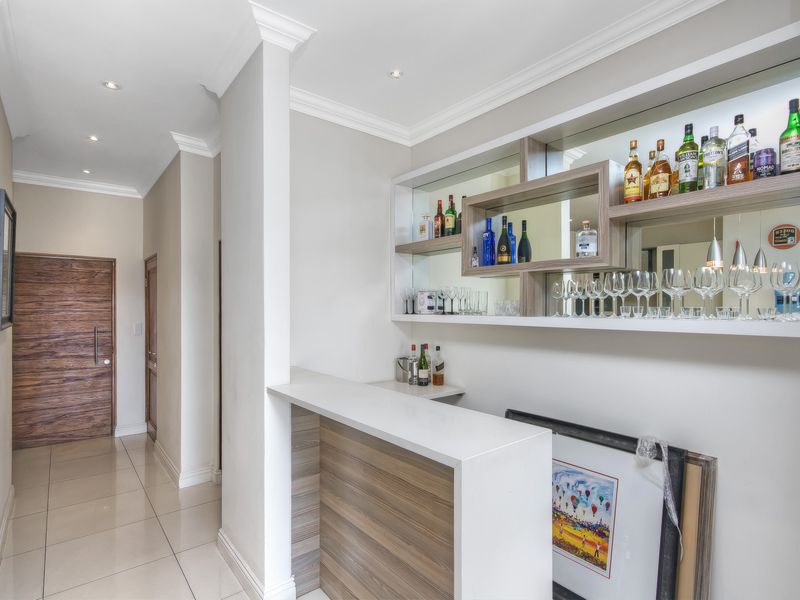 A modern built-in home bar area featuring sleek cabinetry, mirrored shelving with integrated lighting, and polished tile flooring, seamlessly integrated into the hallway space.