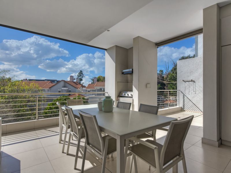 Spacious covered balcony featuring a built-in braai, stainless steel balustrades, and tiled flooring, offering an ideal outdoor entertainment space with pleasant neighbourhood views.