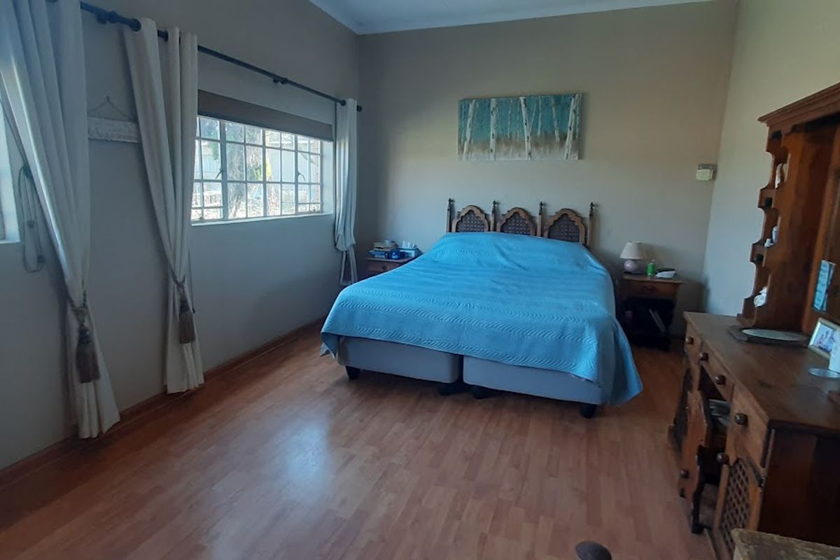 A spacious bedroom featuring laminate flooring, large windows with natural light, and neutral wall tones.