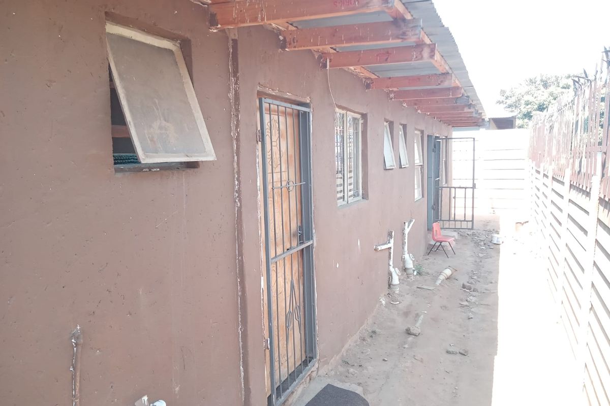 Side exterior view of the property showing exposed roof rafters, security gates, and unfinished ground area along the building perimeter.