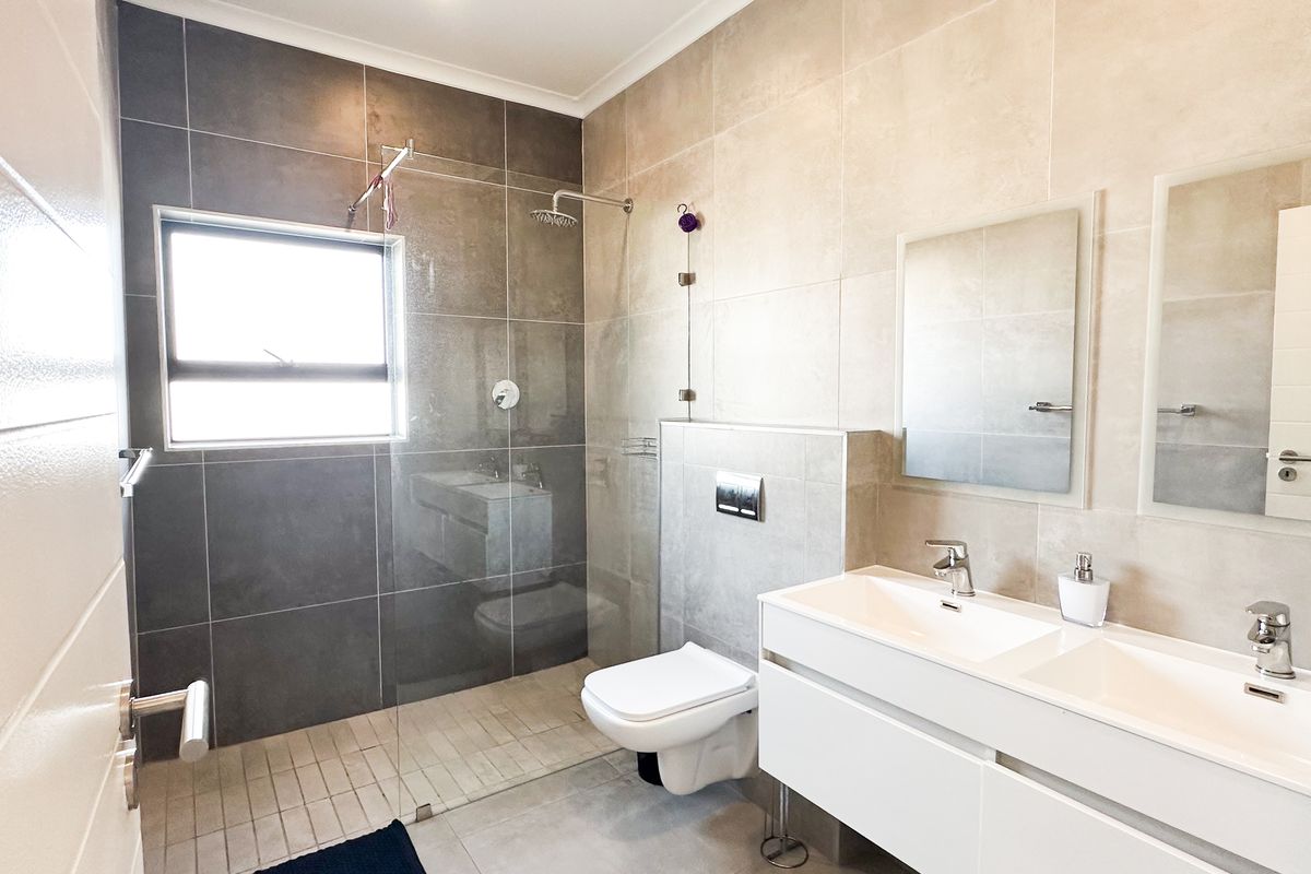 Modern bathroom featuring a double vanity with integrated sinks, a wall-mounted toilet, and a spacious walk-in shower with glass enclosure.