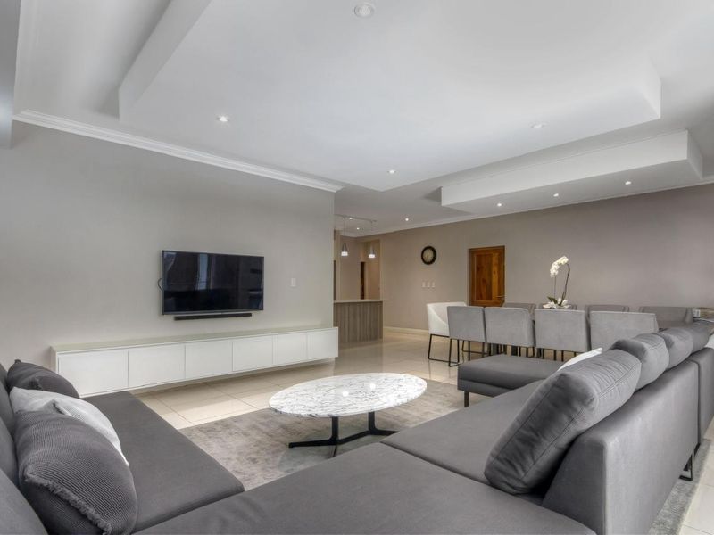 Spacious open-plan living and dining area featuring modern tiled flooring, recessed ceiling details with downlights, and a sleek built-in media console.