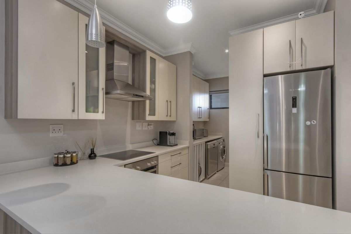 Modern kitchen featuring sleek cabinetry, stone countertops, integrated appliances, and a functional layout with an adjoining laundry area.