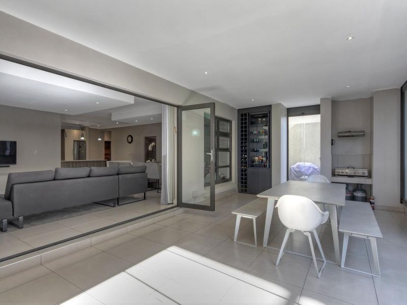 Spacious covered patio featuring tiled flooring, recessed lighting, built-in braai, and a custom wine storage unit, seamlessly connecting to the indoor living area.
