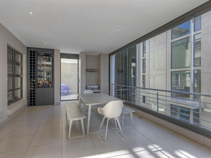 Modern open-plan dining area featuring tiled floors, recessed lighting, and a large glass-enclosed balcony with metal railings and a built-in wine storage unit.