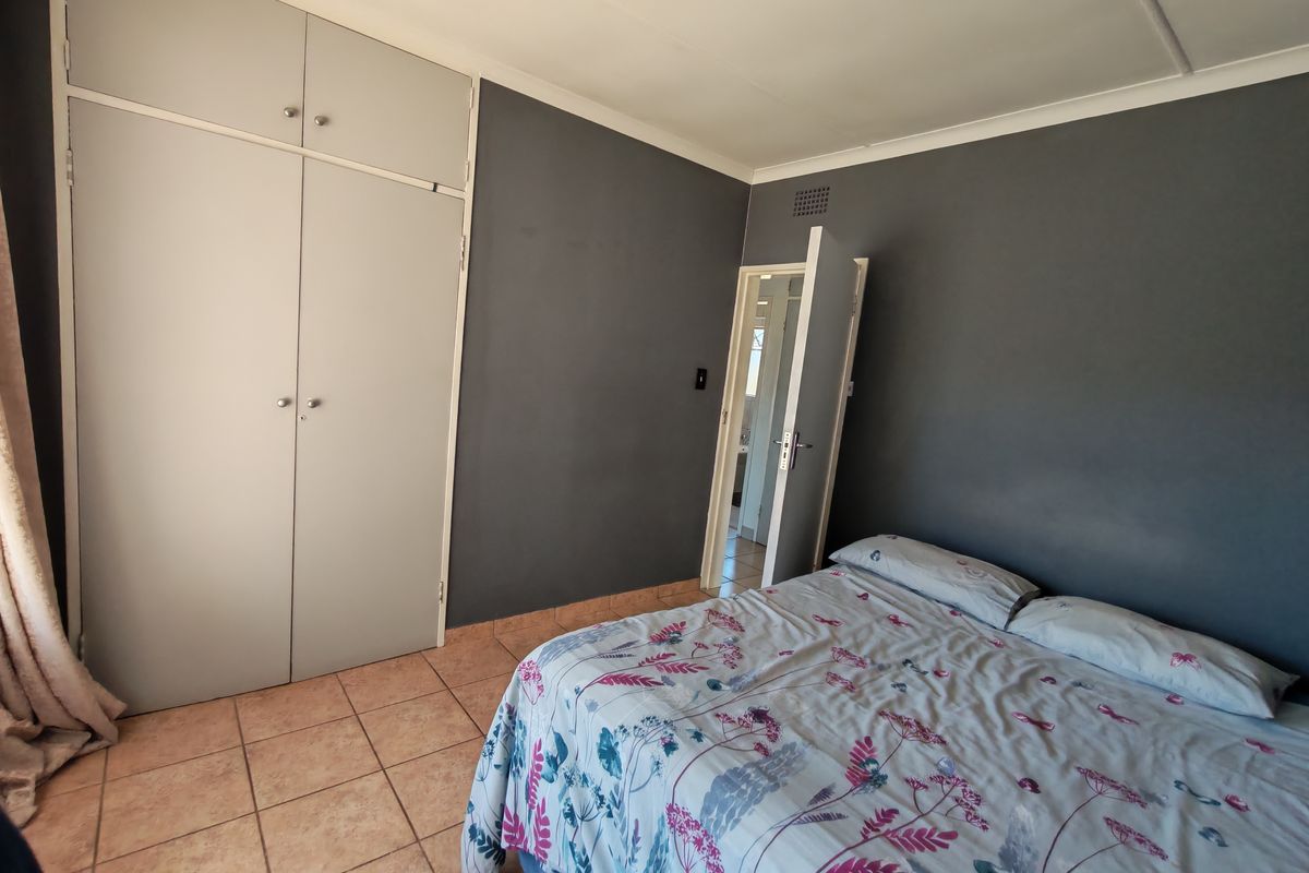 A bedroom featuring built-in cupboards, tiled flooring, and dark grey accent walls, with an adjacent doorway leading to another room.