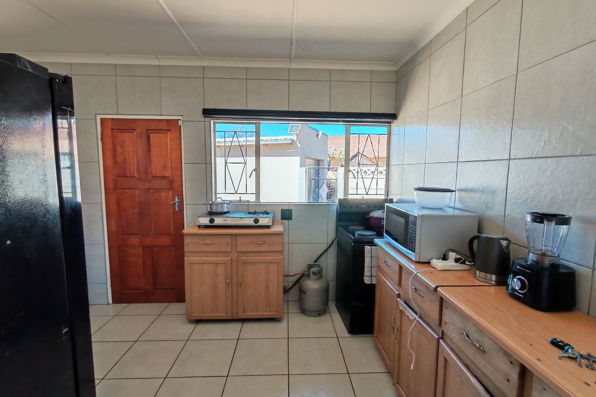 Functional kitchen featuring tiled walls, wooden cabinetry, and a window overlooking the exterior. Includes space for a freestanding stove and gas connection.