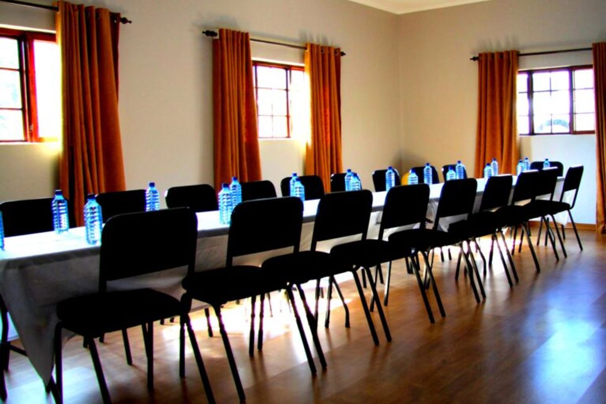 A functional multi-purpose room featuring laminate flooring and multiple timber-framed windows with curtain rods, currently set up for conference or dining use.