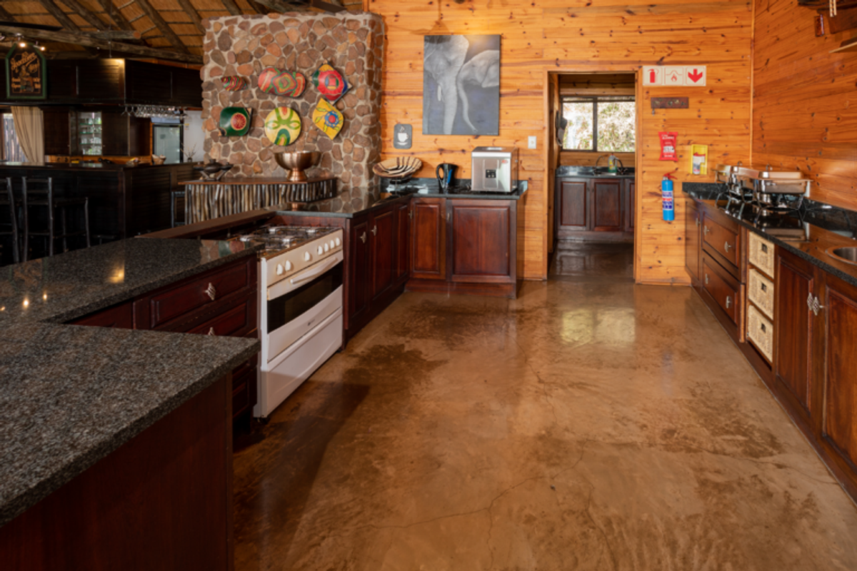 Spacious lodge-style kitchen featuring polished concrete floors, timber wall cladding, a stone feature wall, granite countertops, and a gas stove.