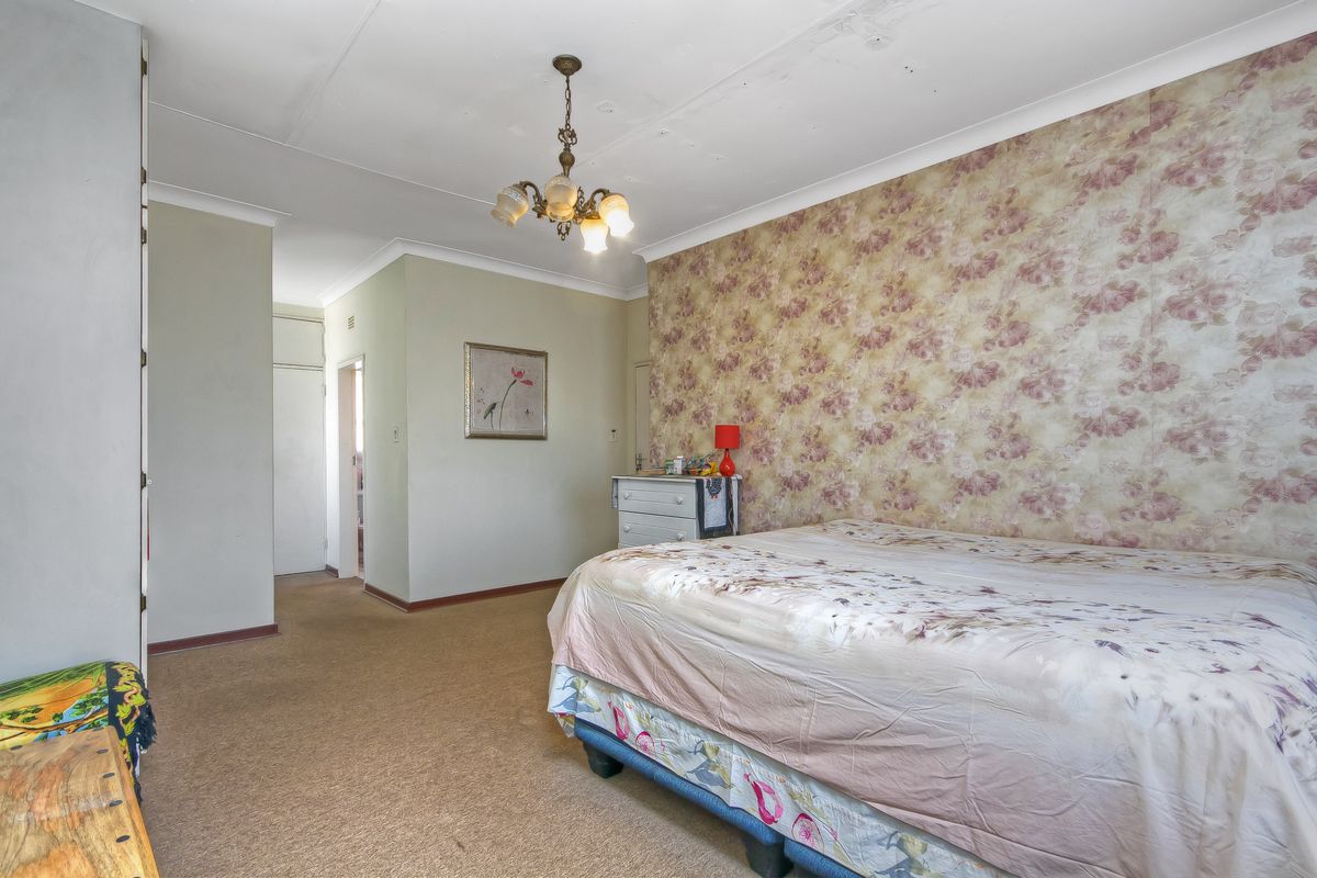 A spacious bedroom featuring floral wallpaper, carpeted flooring, and built-in storage, requiring cosmetic updates to modernize the space.