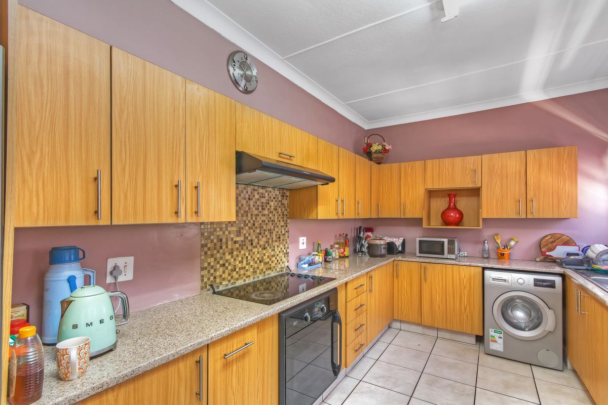 Functional kitchen featuring light wood-finish cabinetry, granite countertops, mosaic tile backsplash, and integrated space for laundry appliances.