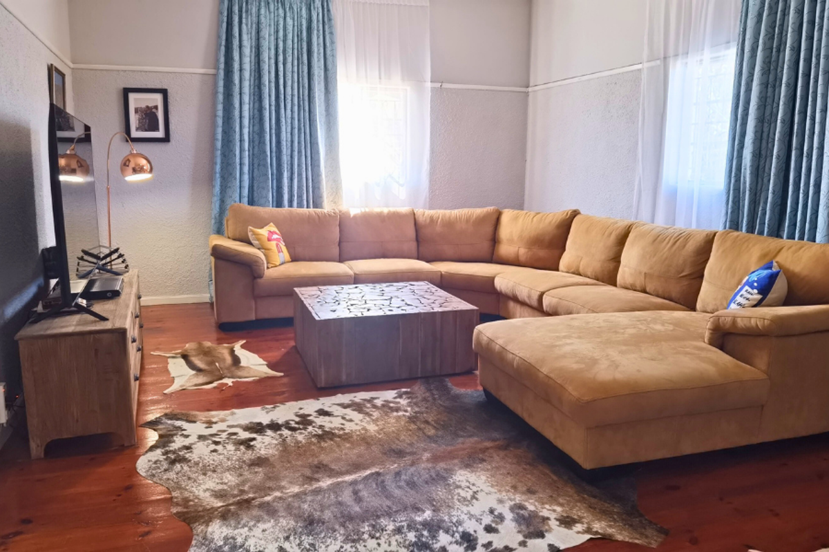 A comfortable living room featuring polished timber flooring, textured wall finishes, and large windows dressed with floor-to-ceiling curtains.