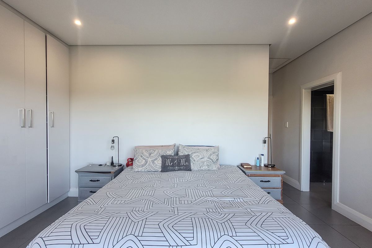 A well-maintained bedroom featuring modern built-in cupboards, neutral tiled flooring, recessed lighting, and direct access to an en-suite bathroom.