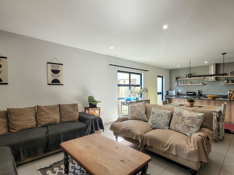 Spacious open-plan living area featuring tiled floors, recessed lighting, and a modern kitchen with timber shelving and a functional island bench.