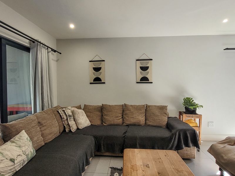 A bright and spacious living room featuring neutral walls, tiled flooring, and large sliding glass doors that provide access to the outdoor area.