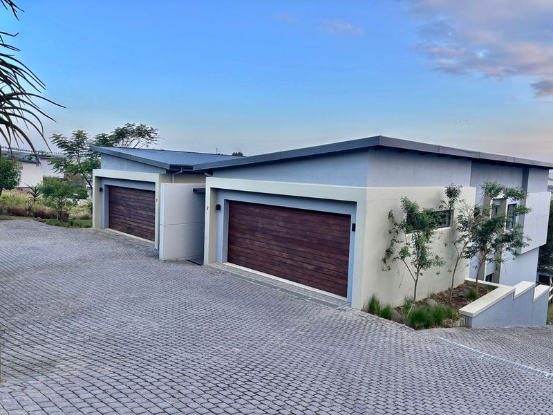 Modern townhouse exterior featuring double garages with timber doors, a paved driveway, and contemporary architectural design with a skillion roof profile.