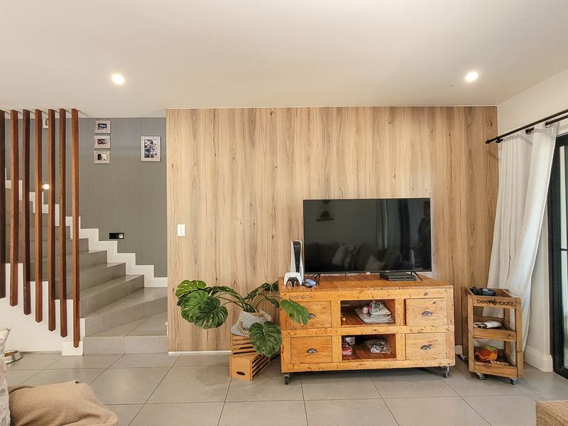 Modern living room featuring a wood-look feature wall, tiled flooring, and a contemporary staircase with timber slat balustrade leading to the upper level.