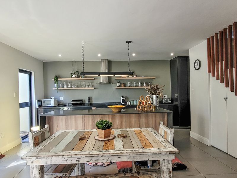 Modern open-plan kitchen featuring a central island, floating shelving, and a distinctive timber slat feature wall, seamlessly integrated with the dining area.