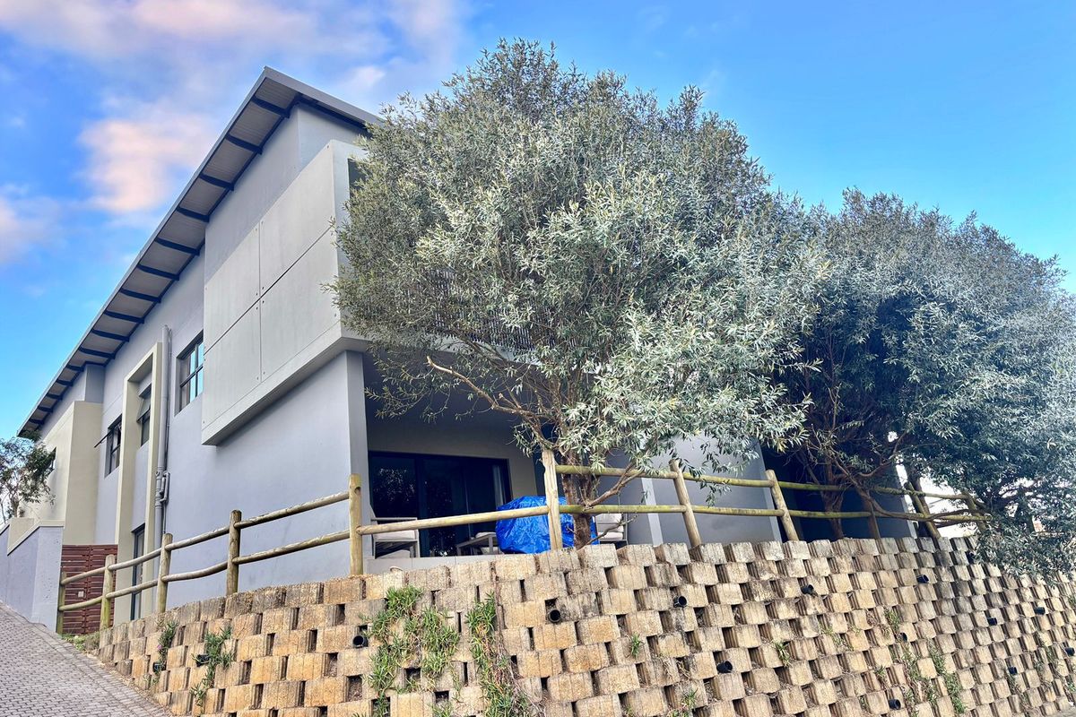 Rear view of a modern townhouse featuring a covered patio, timber fencing, and a tiered concrete block retaining wall.