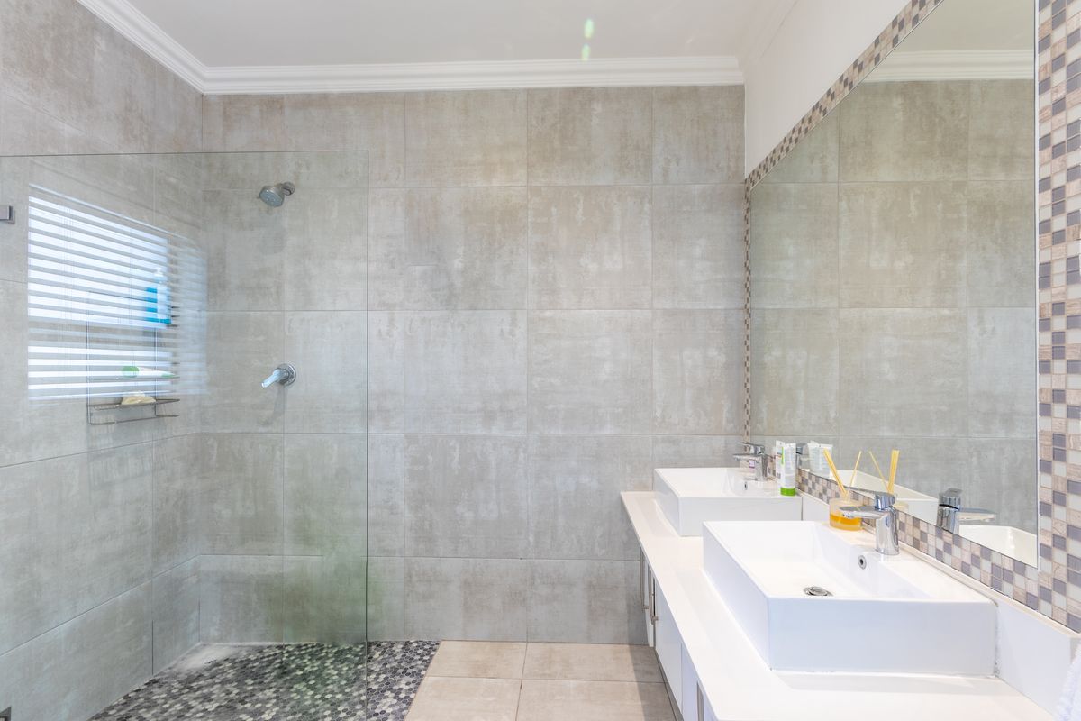 Modern bathroom featuring a frameless glass walk-in shower, dual vessel sinks on a white vanity, and large-format grey wall tiles.